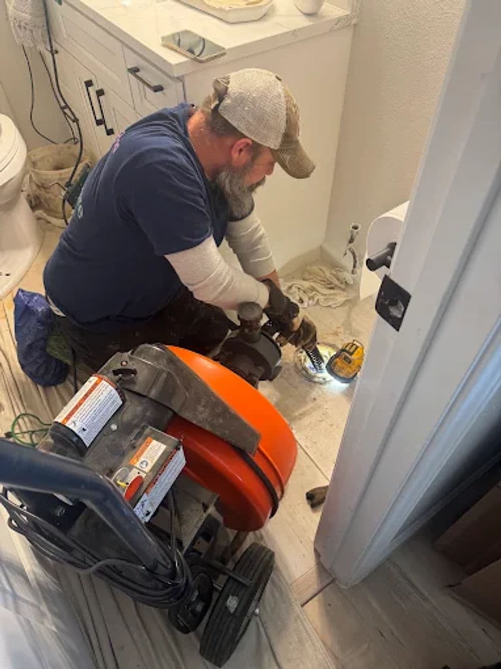 Plumber using a serpentine drain cleaner in a bathroom for maintenance and repair.