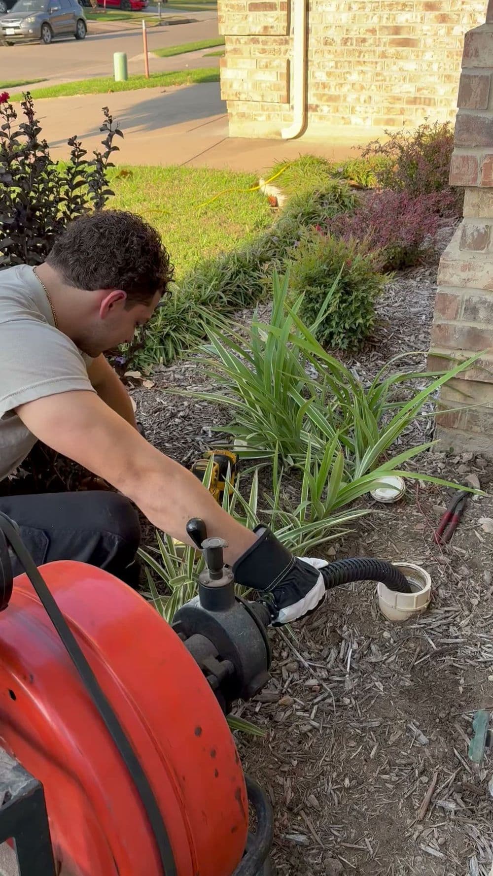Man using a drain auger to clear a blockage in a residential garden landscape.